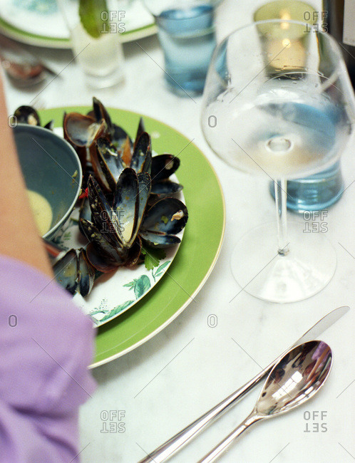 Empty mussel shells on green rimmed plate with purple sleeve on diner's arm