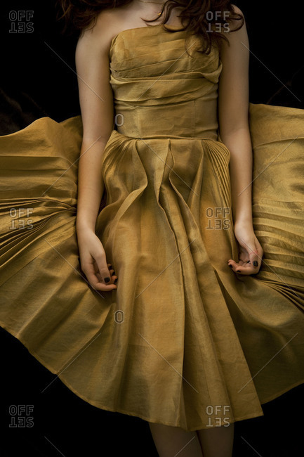 Young girl seen from neck down in vintage gold dress on black background
