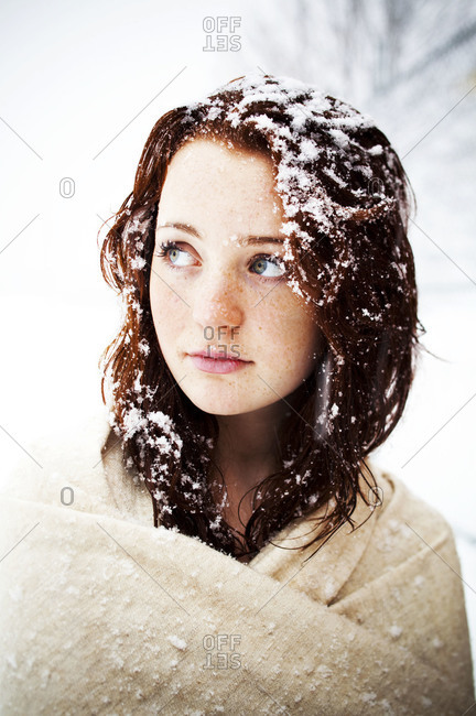Young girl wrapped in beige pashmina shawl in snowstorm.  Hair covered in snow flakes.
