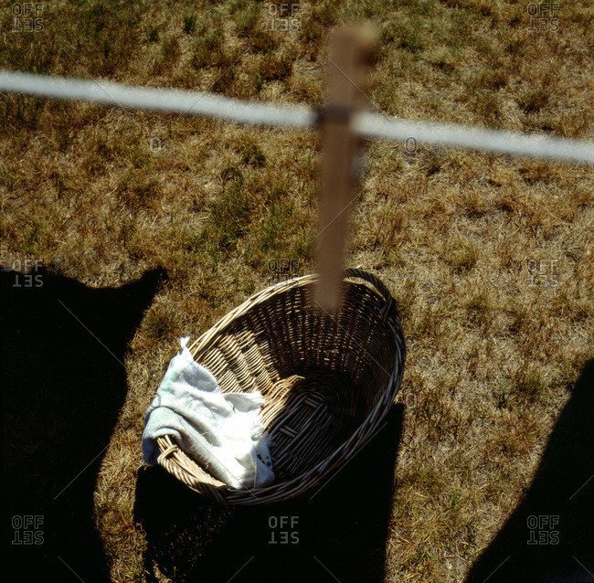 Laundry basket on dry grass seen from above with laundry line, clothespin and sheet shadows pictured