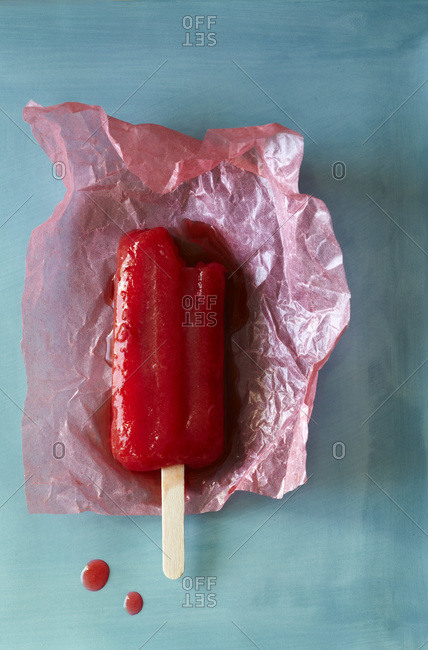 Melting red ice lolly on pink wax paper on sky blue background