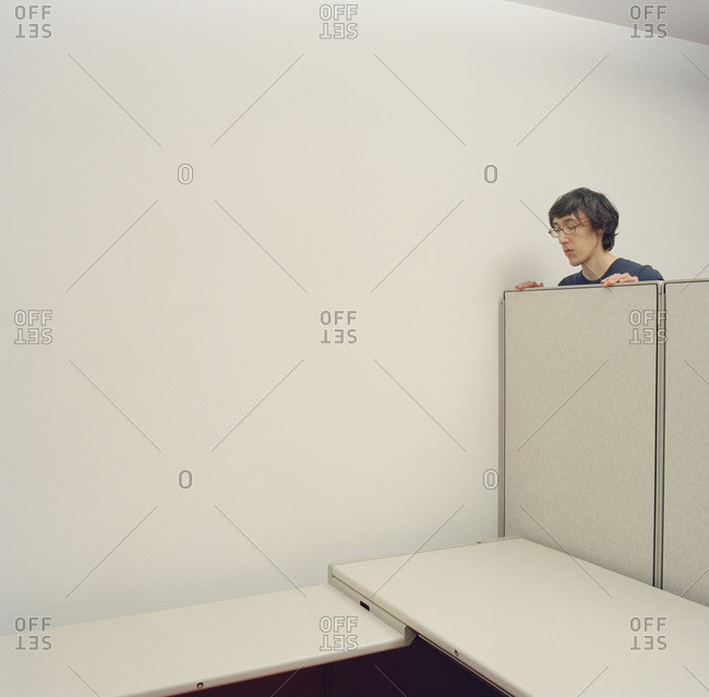 Young man looking over partition wall in empty cubicle