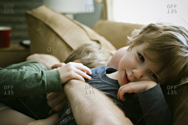 Boys being hugged by their father on couch.