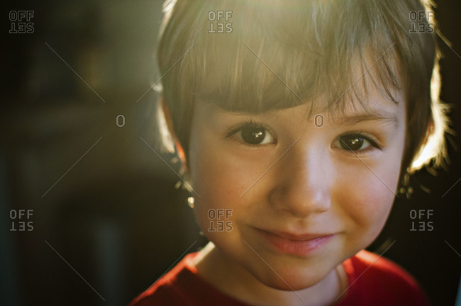 young boy smiling at the camera with sun behind him