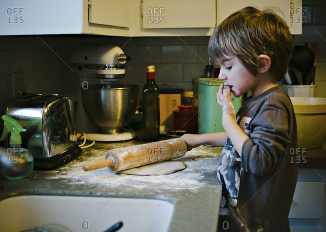 Boy rolling dough on kitchen counter and tasting the flour on his fingers