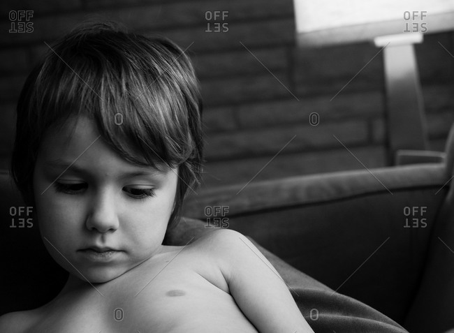 Shirtless boy laying on couch starting down in thought