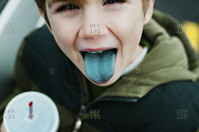 Boy sticking out a stained blue tongue while holding a drink in his hand