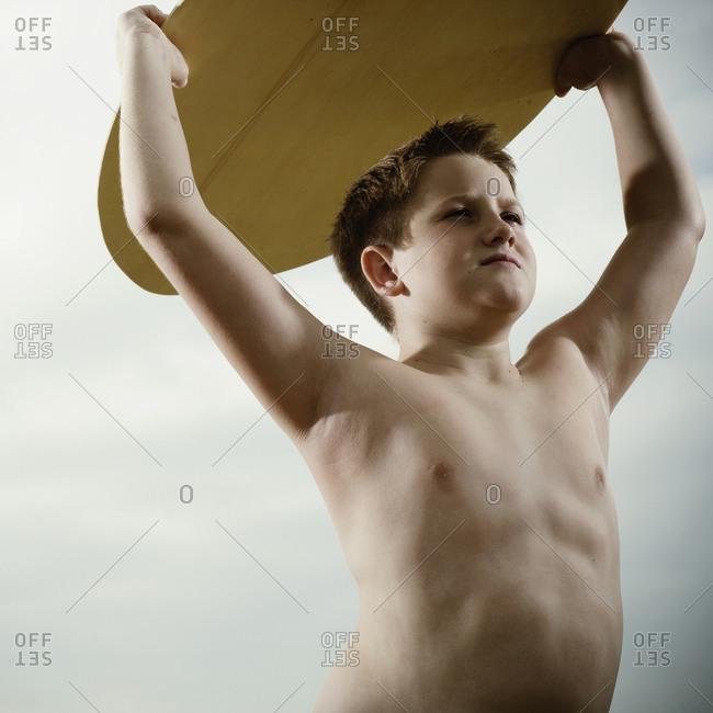 Young boy holding a surfboard over his head