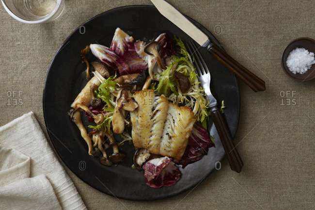 Roasted white fish fish fillet meal with radicchio, mushroom and frisee in a black plate from above