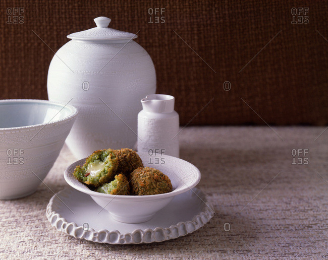 Deep fried broccoli balls in a white ceramic bowl on a table and different kind of cutlery.