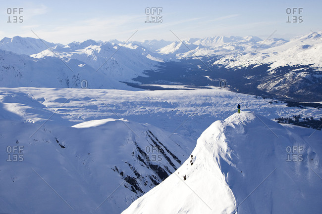 A male skier stands alone on top of a big, remote mountain in Haines, Alaska