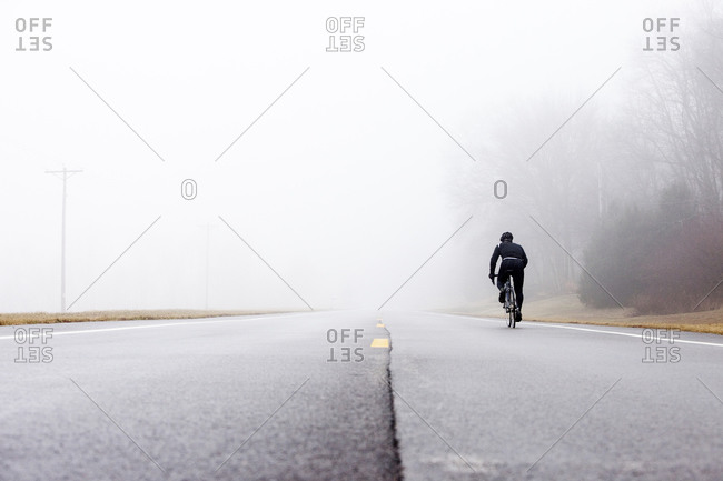 Low angle perspective of one man cycling into a foggy background