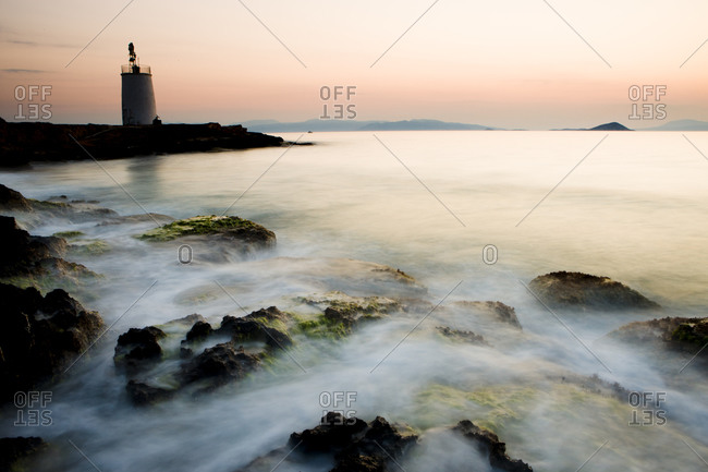 Lighthouse at sunset with waves splashing in the foreground near Aegina, Greece