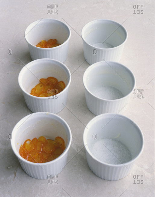Six pie pots on a counter. Half of them are empty and other half with a layer of cumquats at the bottom