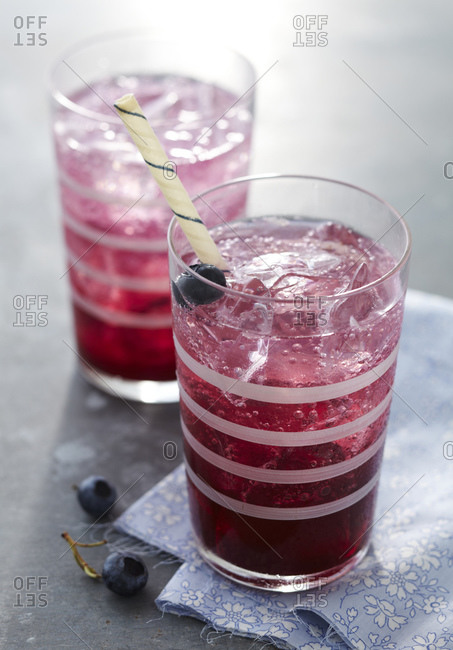 Blueberry syrup with sparkling water, ice cubes and straw.