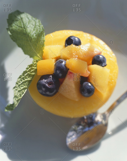 Halved fresh peach filled with raw blueberries and peach cubes, decorated with mint leaves.