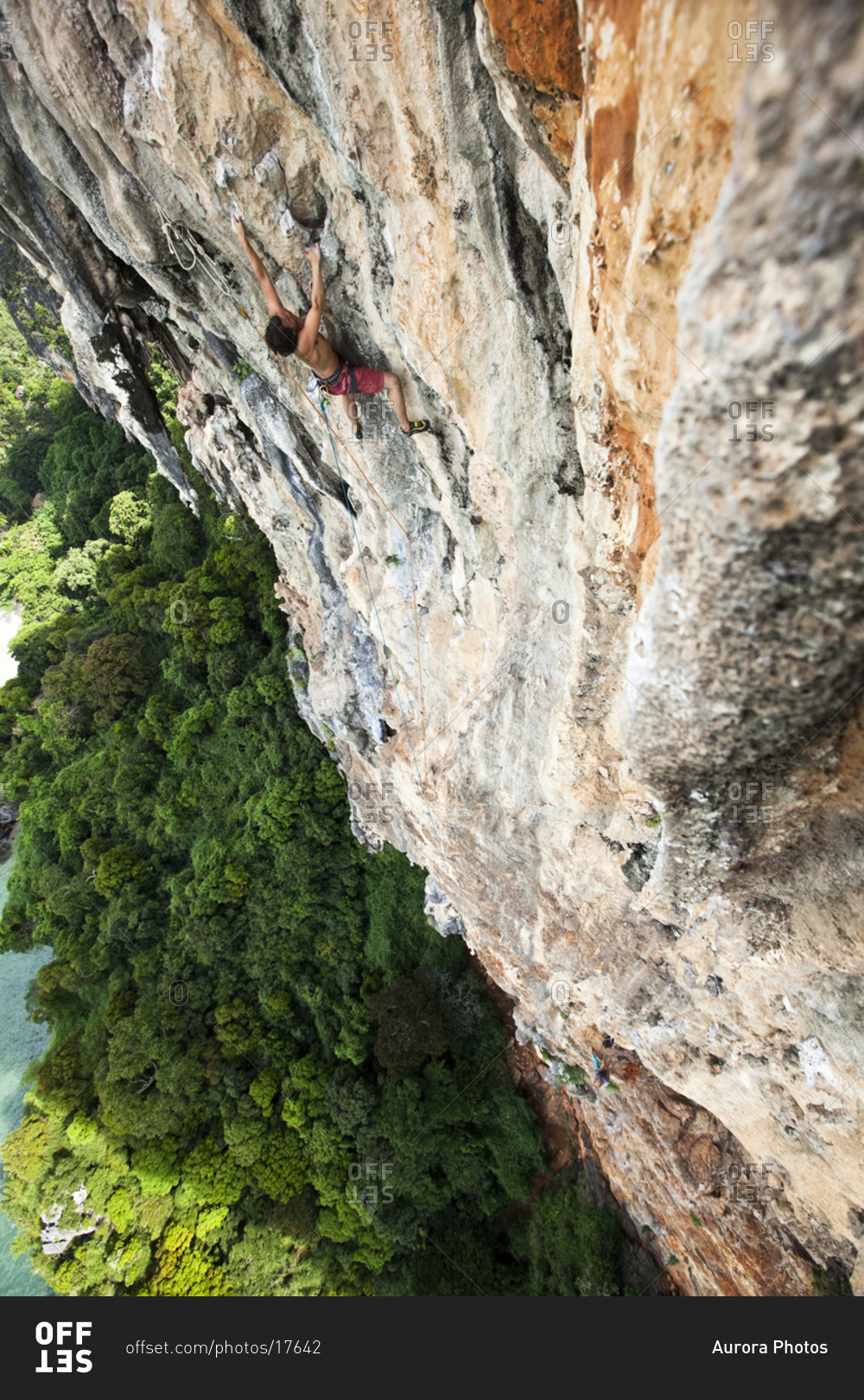 A athletic man rock climbing high above the trees and water on a multi ...