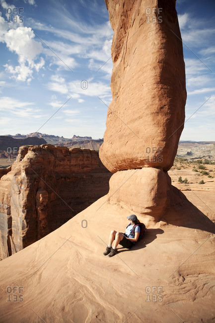 A female hiker rests against Delicate Arch in Arches National Park, Utah.