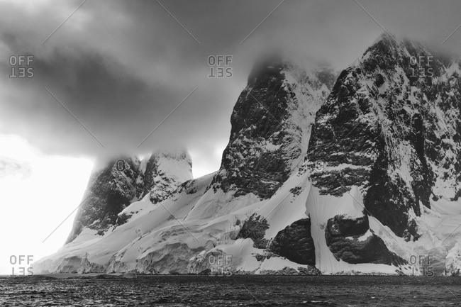 Dramatic Antarctic sky above water and mountain in black and white
