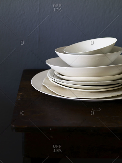 Pile of clean empty plates and bowls on a wooden table.