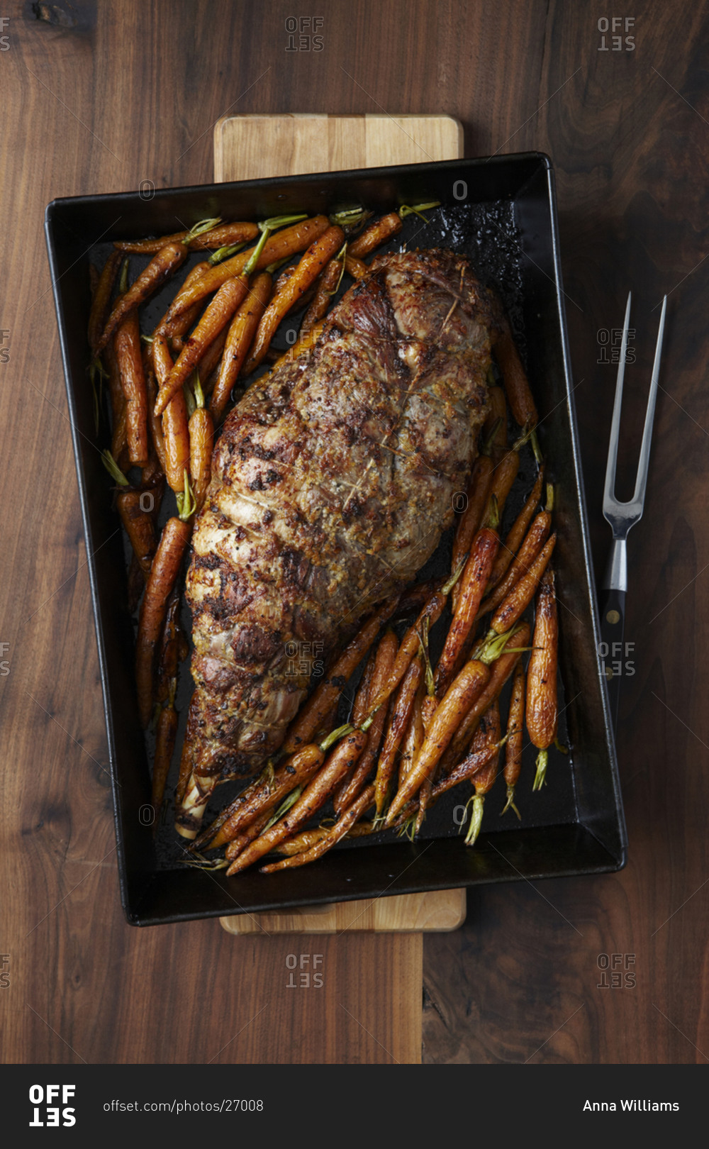 Roasted leg of lamb seasoned and tied together in a pan with roasted carrots