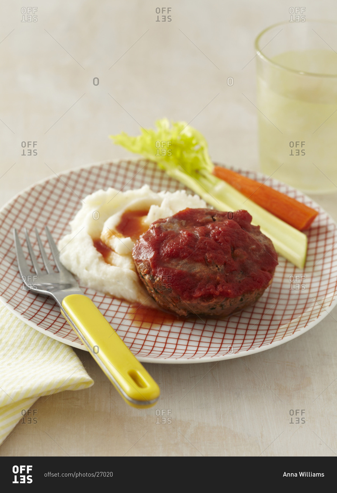 A child's plate with a meat loaf patty covered with tomato sauce, mashed potatoes with a celery and carrot stick