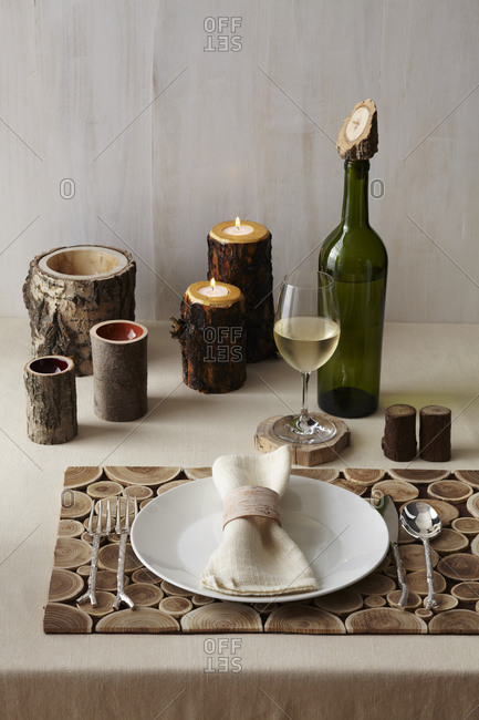 A wood themed table place setting with a wooden place mat, wooden salt and pepper shakers, wooden candle holders, wooden cups, a wooden coaster and a wooden wine corker