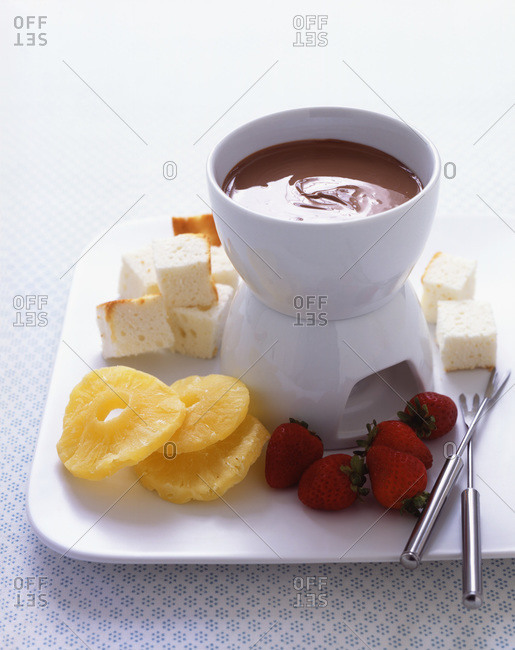 Chocolate fondue with dried pineapple slices, fresh strawberries and bread cut into cubes for dipping, with two small dipping skewers