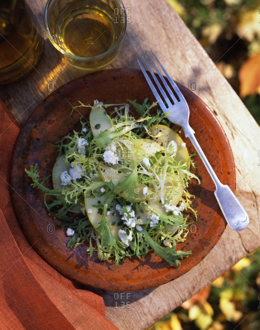 Salad with pear slices and goat cheese sitting on a table outside