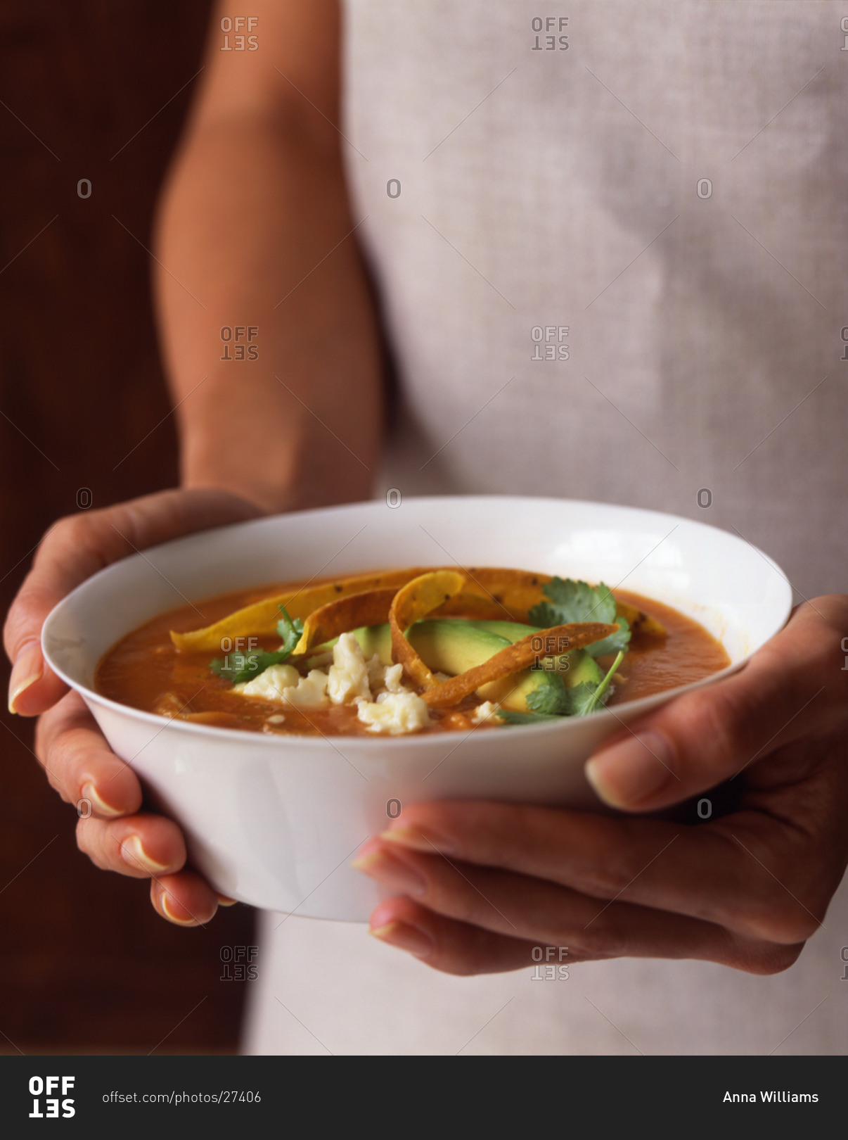 Woman holding a bowl of spicy Mexican tortilla soup topped with tortilla strips
