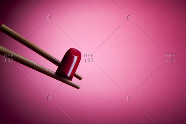 Red lipstick bullet being held by chopsticks