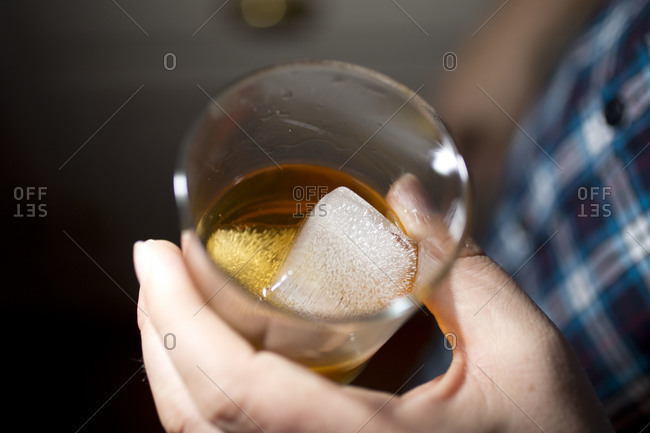Glass of alcoholic beverage with ice cube, closeup