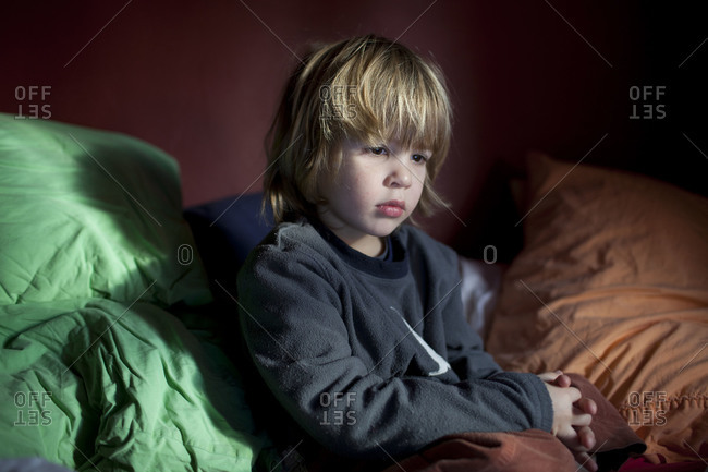 Sleepy toddler sitting on blanket in the bed.