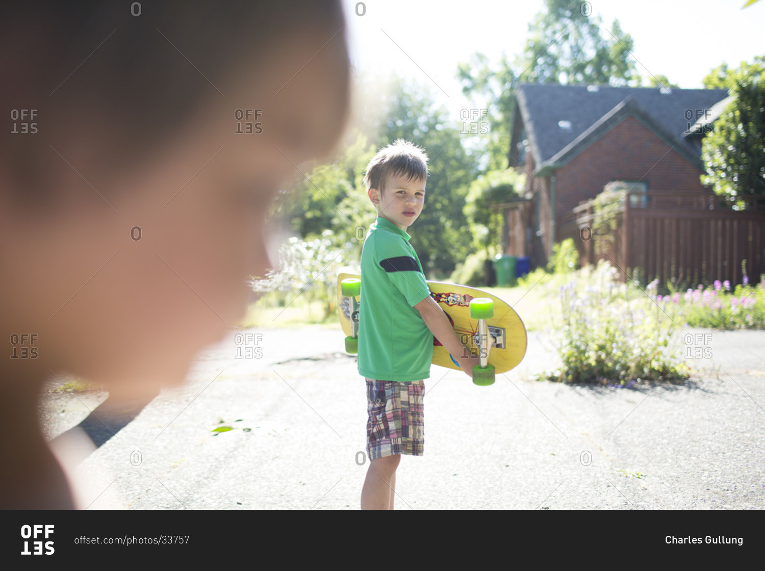 Little boy holding his skateboard looking at another child