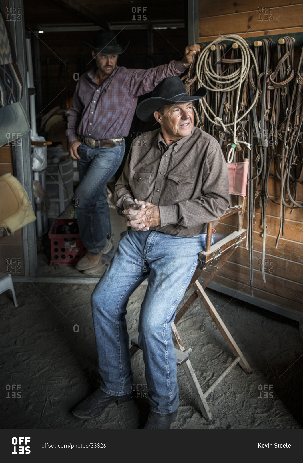 Two middle aged cowboys sitting at stable stock photo - OFFSET