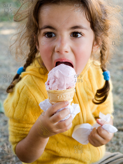Young girl eating strawberry ice cream from a cone