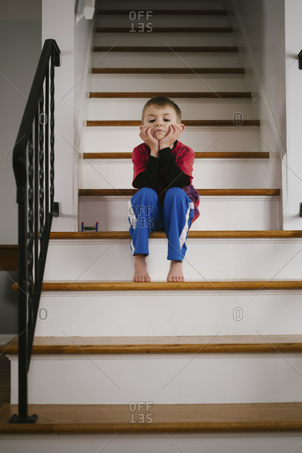 A barefoot little boy sitting on a staircase