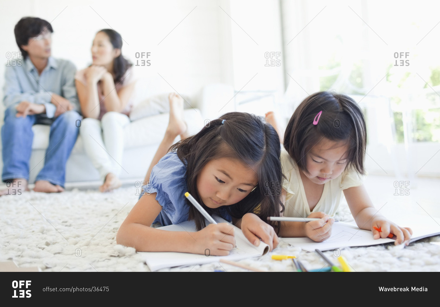 The parents chat on the couch as the girls lie on the ground and color in their coloring books