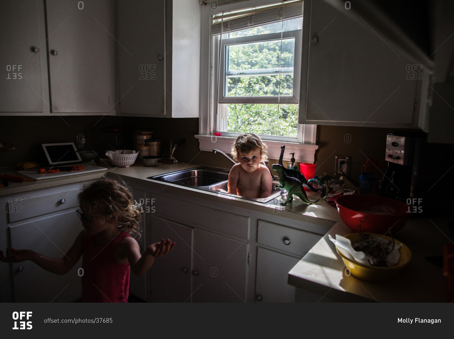 a child takes a bath in kitchen sink while a child dances