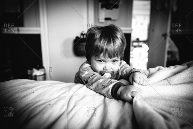 1 year old boy with pacifier in mouth grabs blanket on bed