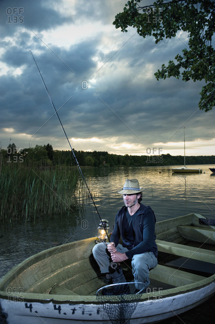 Germany, Bavaria, Woerthsee, Man with lantern fishing in boat at dusk