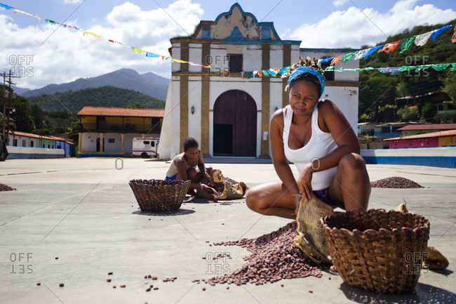 Two women rake cacao beans into a pile in front of the town church in the small, remote village of chuao, venezuela