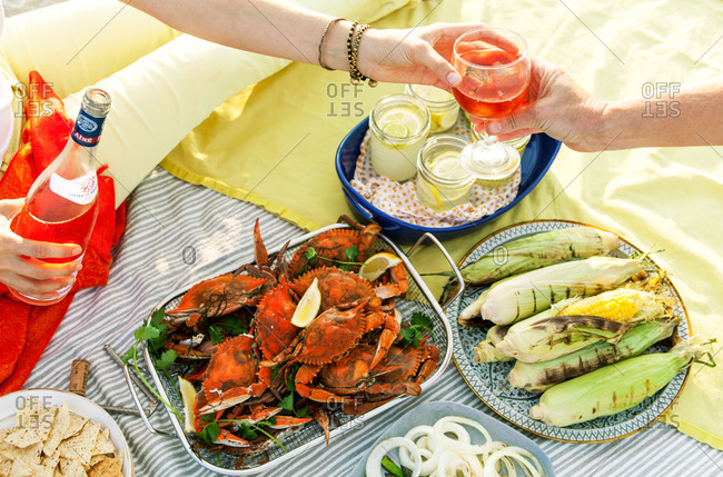 Close up of couple sitting with grilled foods and drinks on picnic blanket