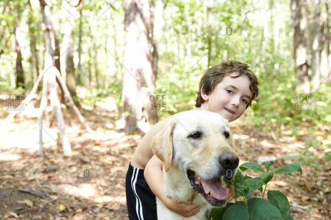 Young Caucasian boy walking with big Labrador in forest