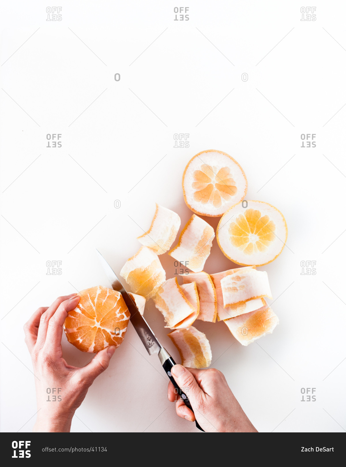 Hands peeling orange with knife on white background
