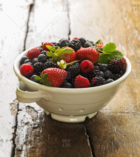 Fresh berries in ceramic strainer on vintage wooden surface.