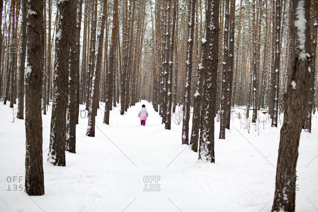 A young girl walking down a snow packed path in the forest