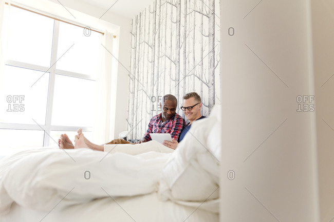 Gay couple sitting in bed and using tablet computer