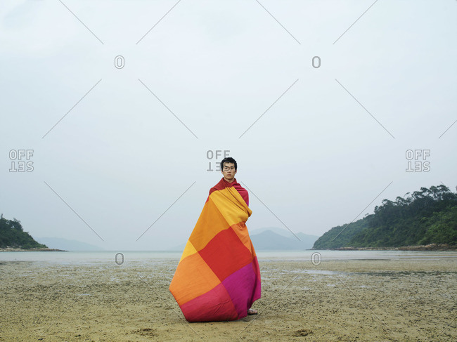 Man wrapped in blanket, standing on beach