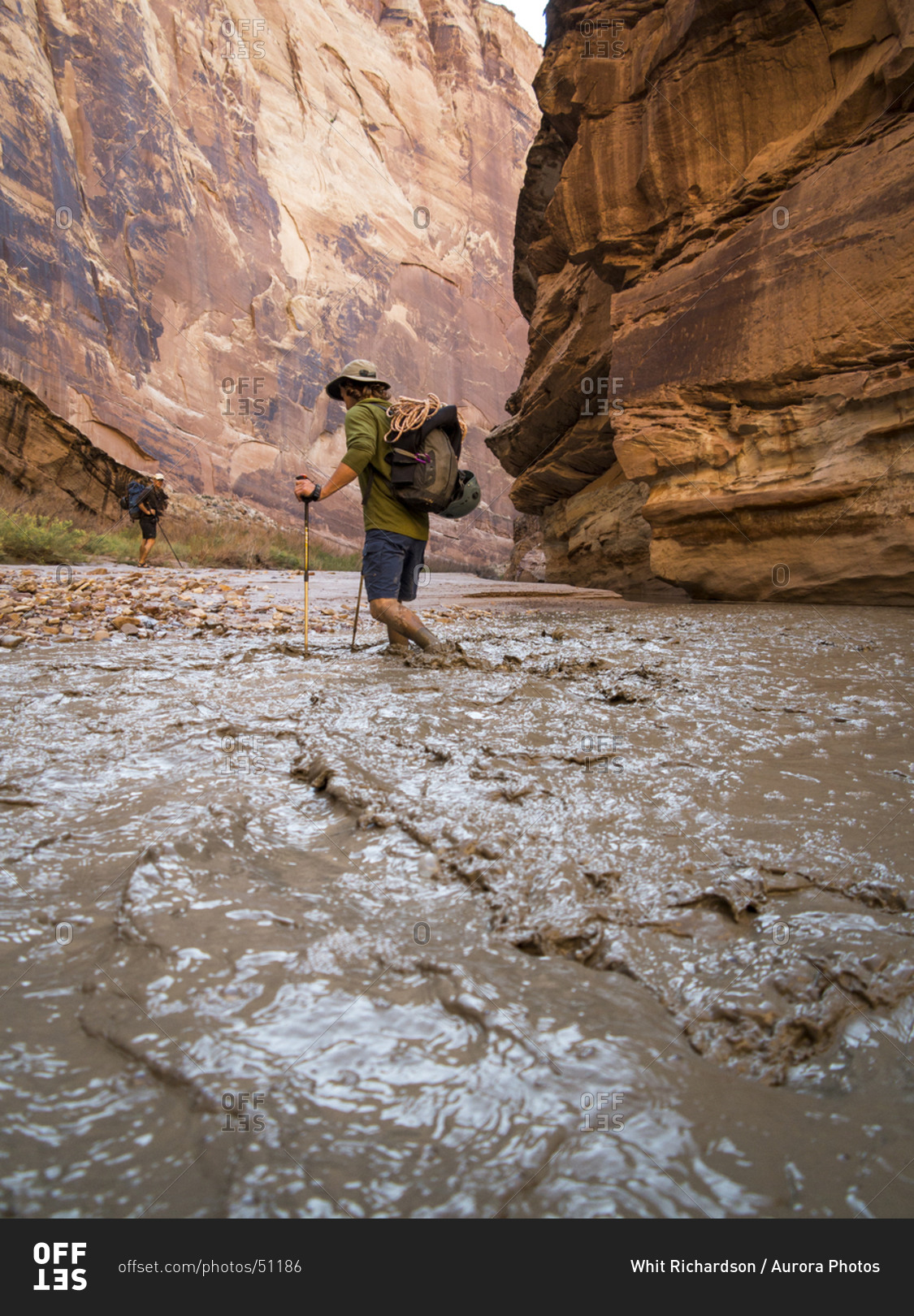 A man hiking through a muddy creek in a canyon.